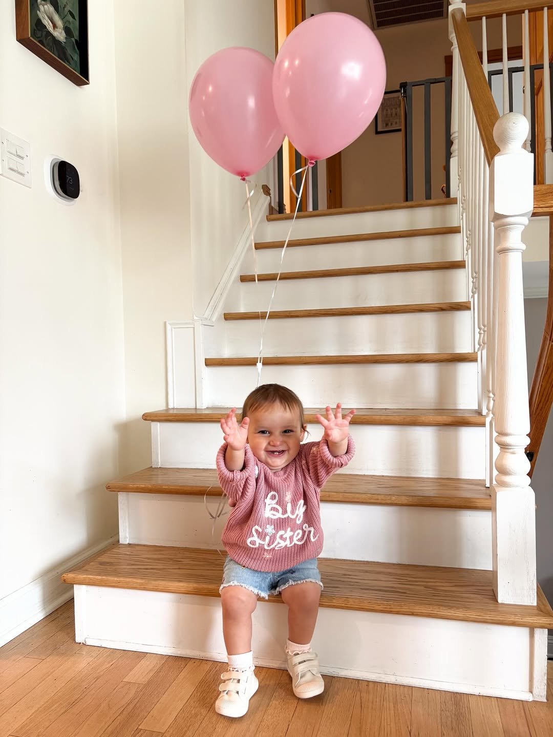 Avery in a Big Sister sweater with pink balloons on the stairs